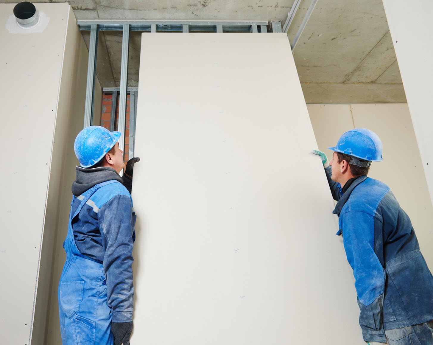 Two construction workers put a sheet of plasterboard into place