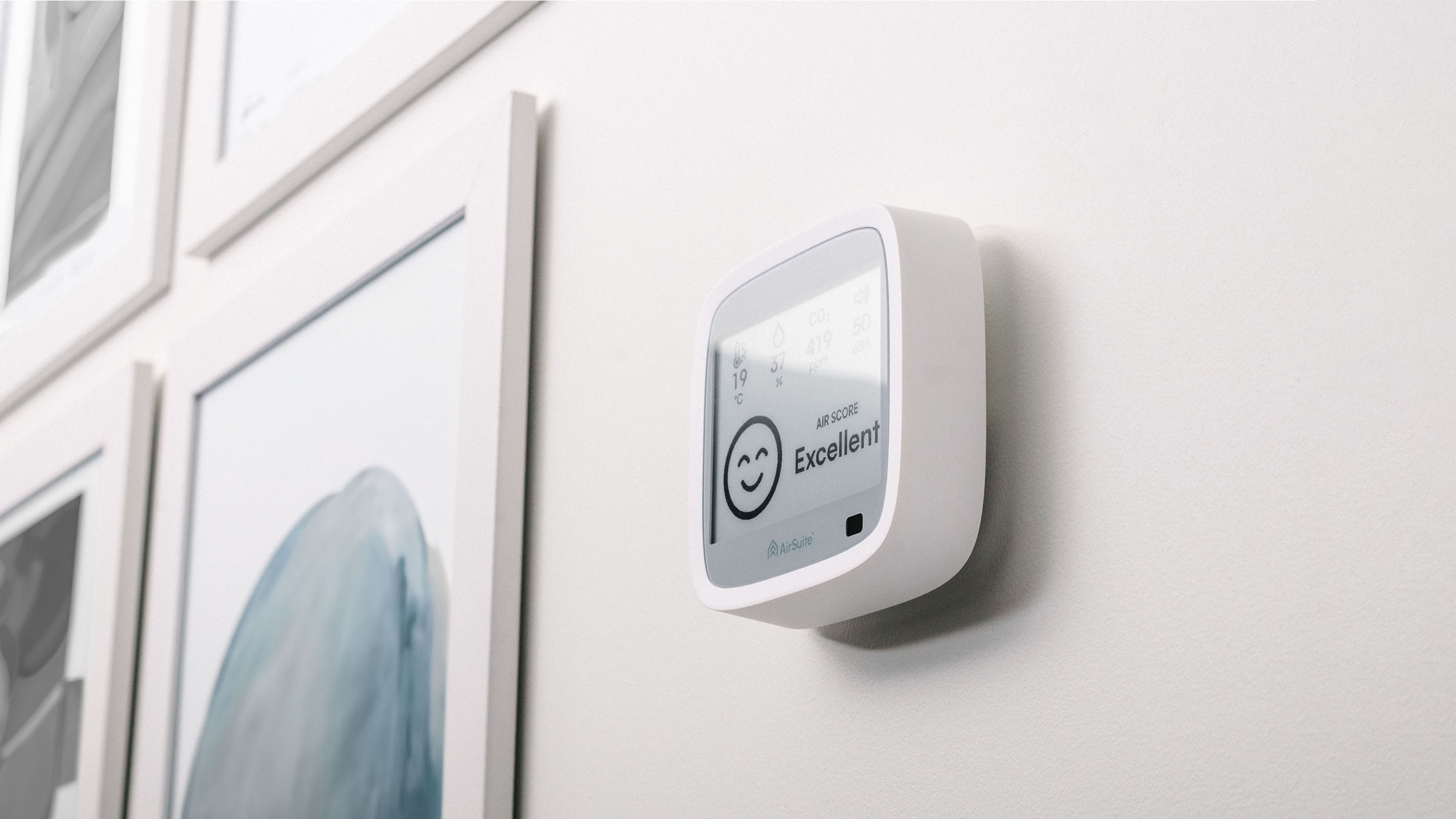 An AirSuite Glance device mounted on the wall next to some picture frames